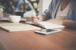 a person holding a pen and writing on a notebook